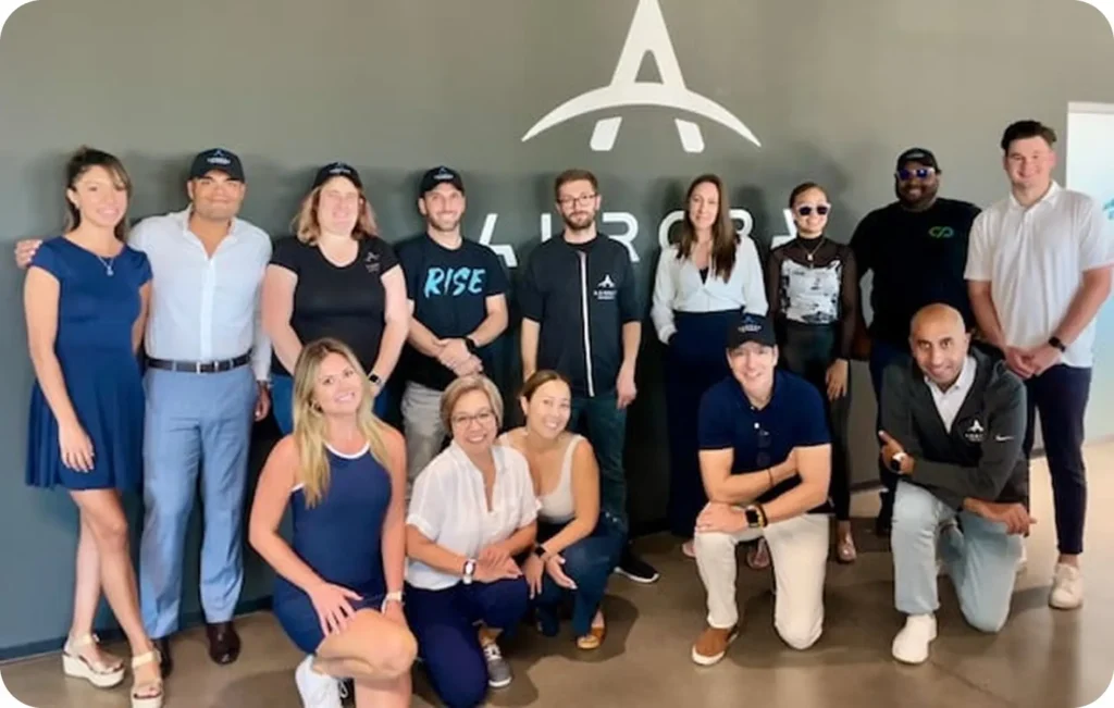 A group photo of the Aurora Payments team standing in front of the company logo.